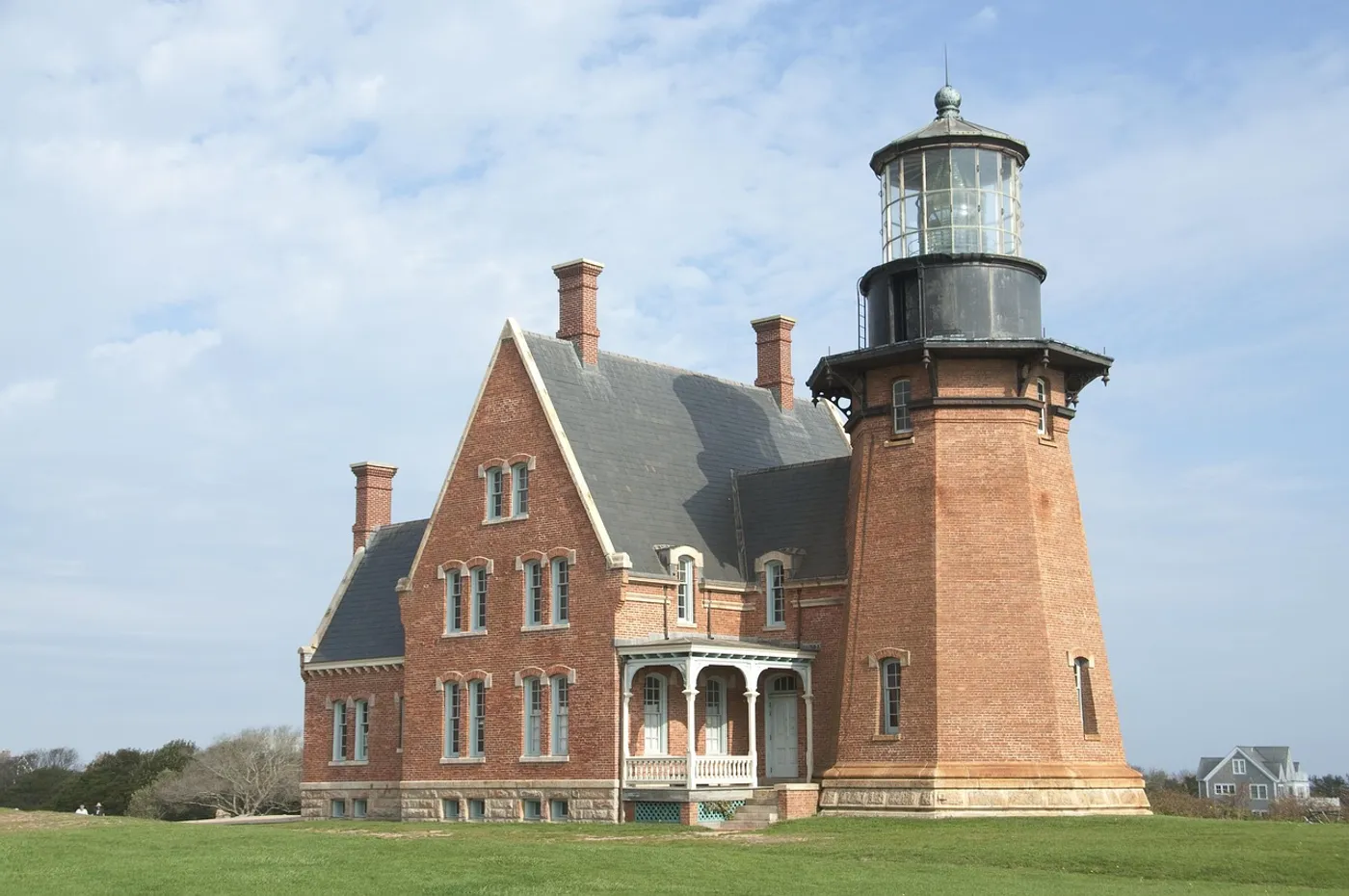 The Southeast Lighthouse: a red-brick Victorian keeper's house and attached tower under a blue sky, seen across its lawn on the bluff.